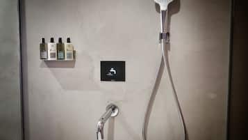 Un espacio de ducha con cabezal de ducha de mano, grifo empotrado en la pared y repisas con artículos de tocador.