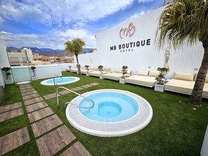 Un área de piscina en la azotea con dos jacuzzis, sillas de descanso y una pared con el logotipo del MB Boutique Hotel.