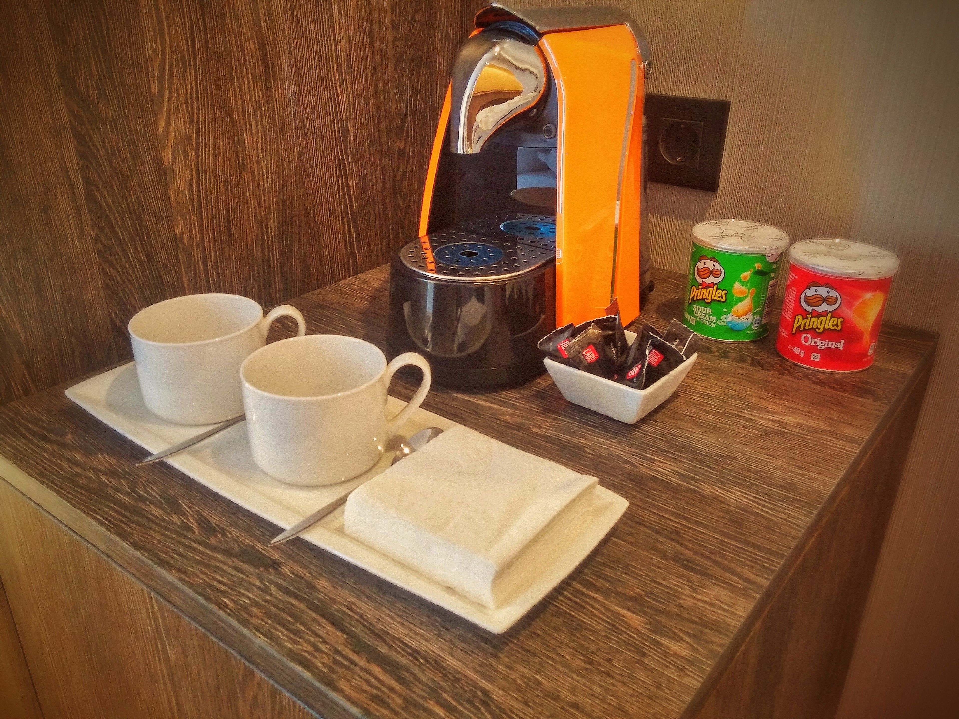 A breakfast tray with two white cups, a spoon, a napkin, a coffee maker, and two Pringles cans.