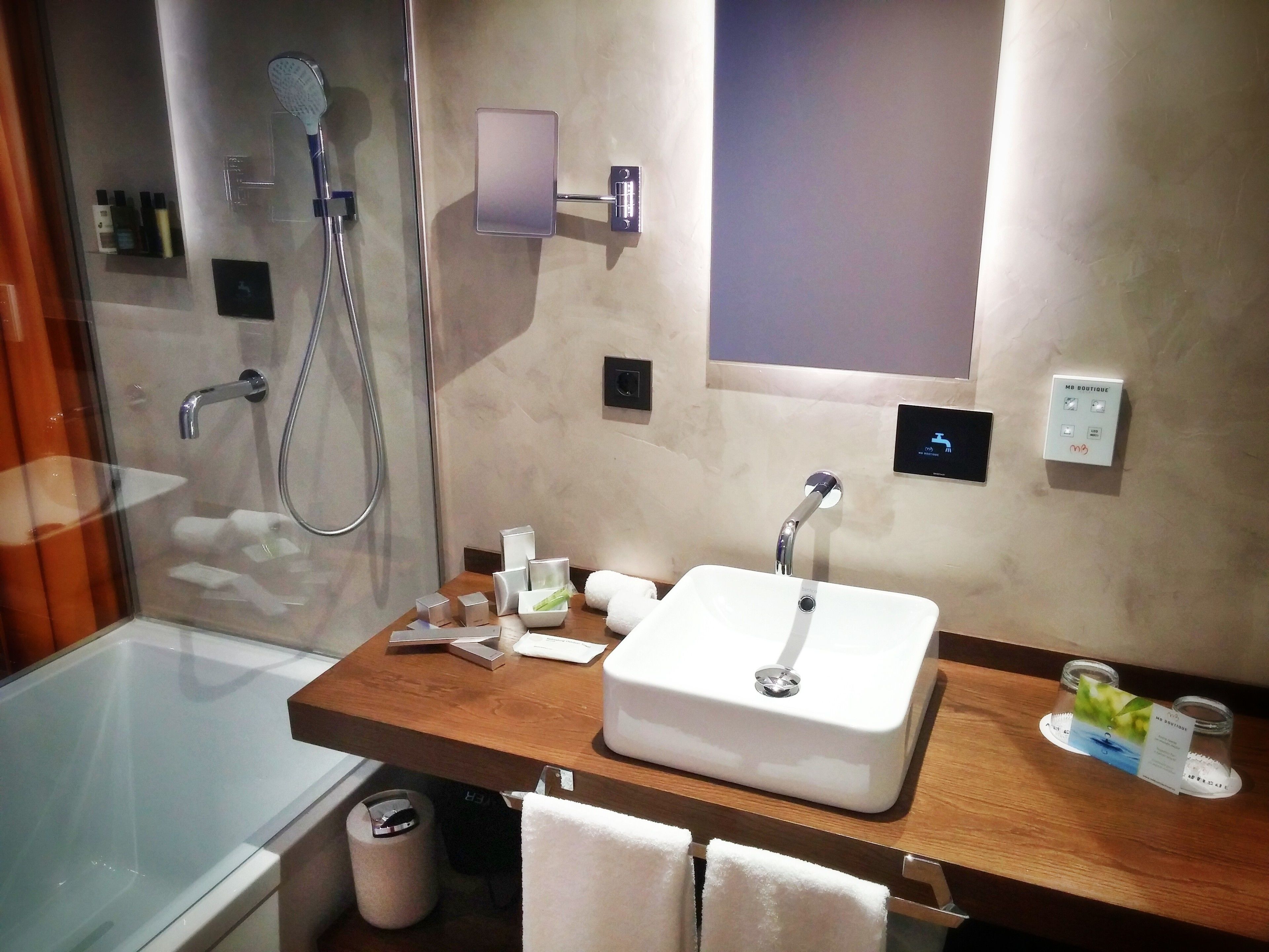 Un baño moderno con ducha de vidrio, tocador de madera con lavamanos blanco y un perchero para toallas.