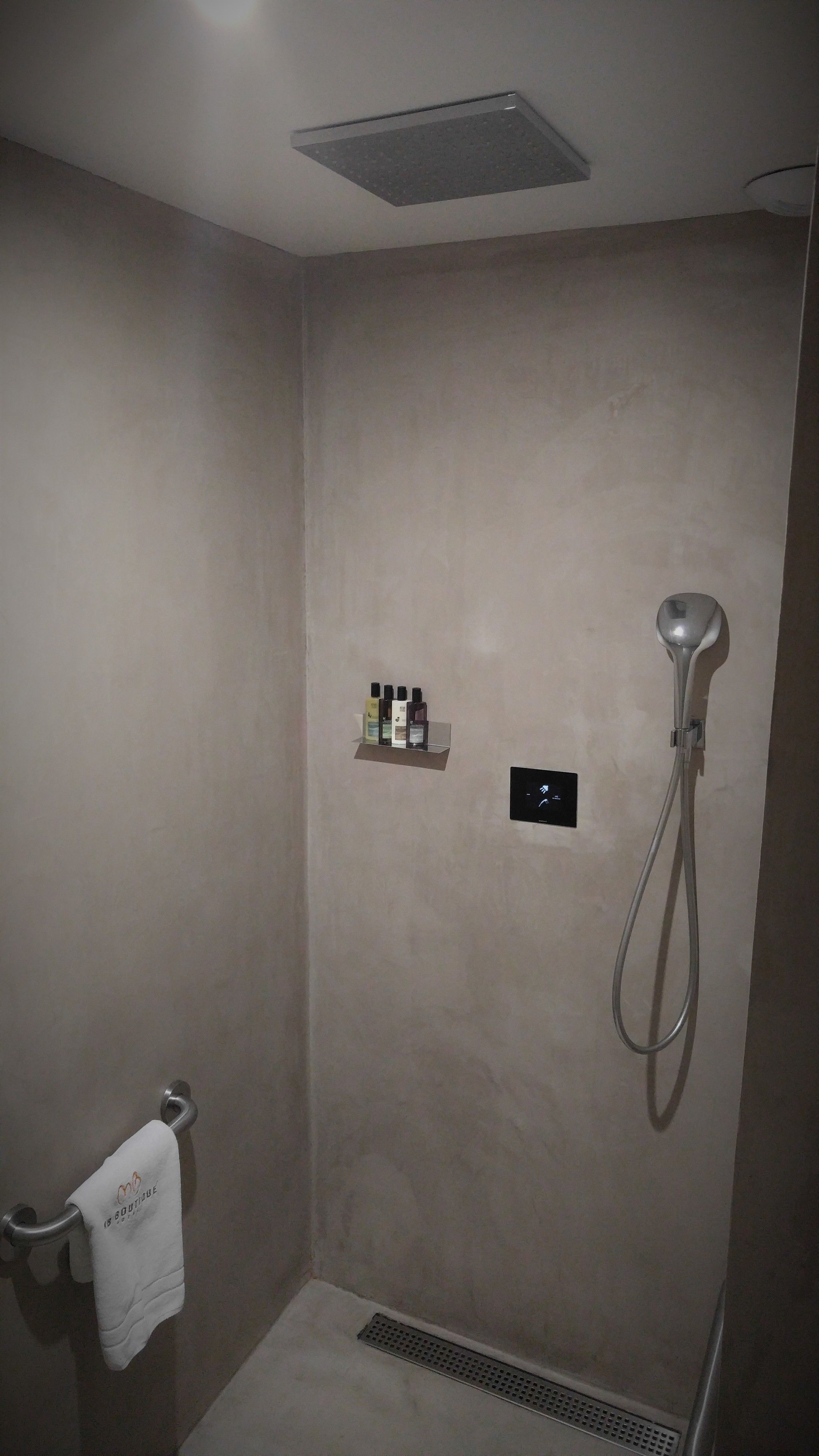A bathroom with a shower, a towel rack, and a shelf with toiletries.