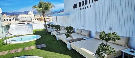 A modern outdoor area with a pool, lounge seating, and a wall with the MB Boutique Hotel logo.