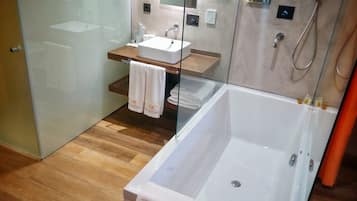 A modern bathroom with a glass shower enclosure, a wooden vanity, and a large bathtub.