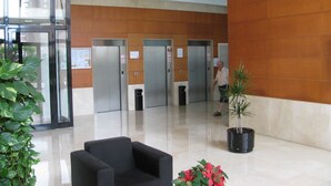 A lobby with three elevators, a black armchair, and potted plants. - Torre Ipanema Apartamentos (Benidorm)