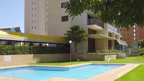 A swimming pool area with two pools, surrounded by a brick patio and a small grassy area. - Torre Ipanema Apartamentos (Benidorm)