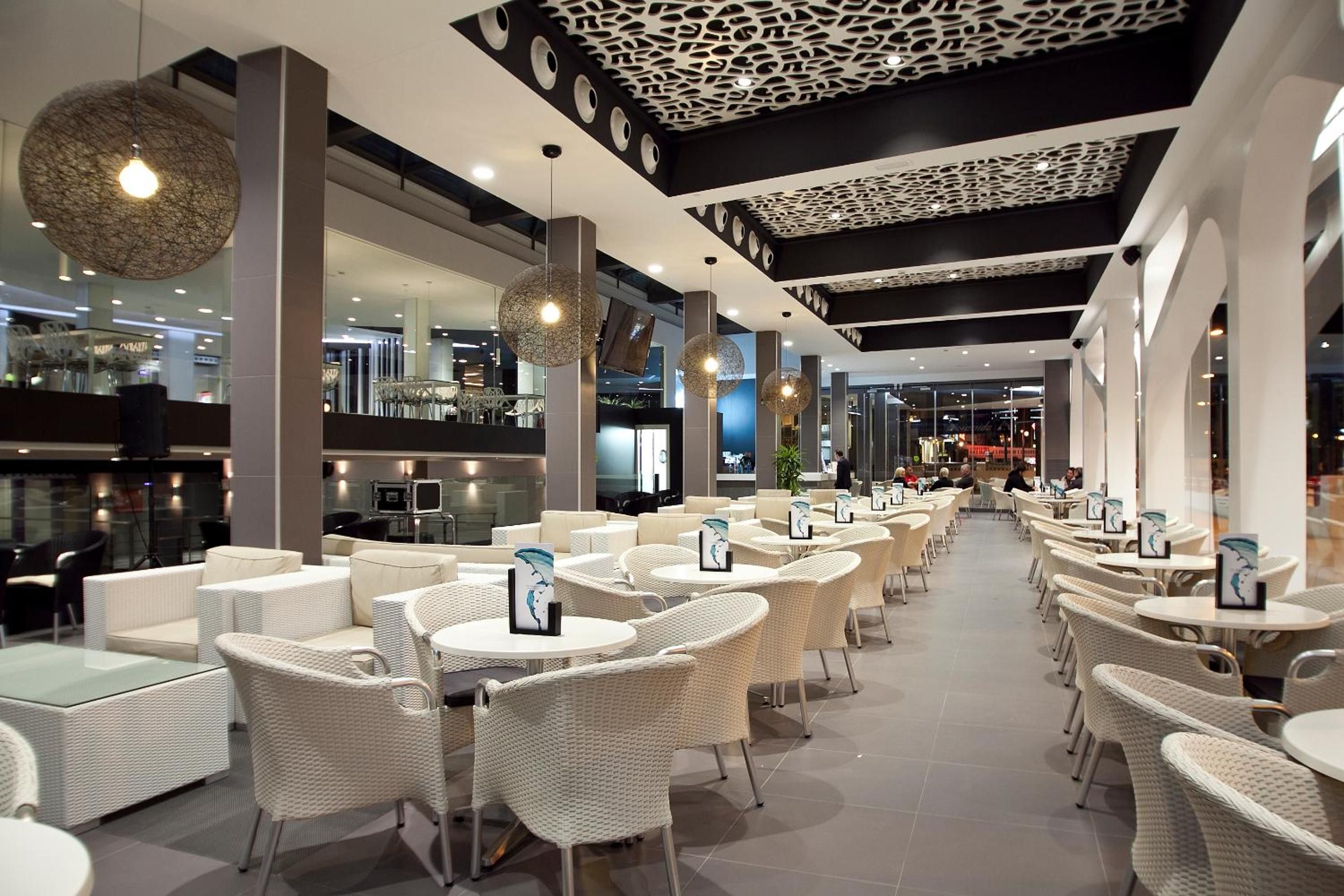 A modern indoor cafe with wicker furniture and pendant lighting.