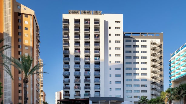 A swimming pool with lounge chairs and umbrellas, surrounded by tall buildings. - Flash Hotel – Adults recommended (Benidorm)