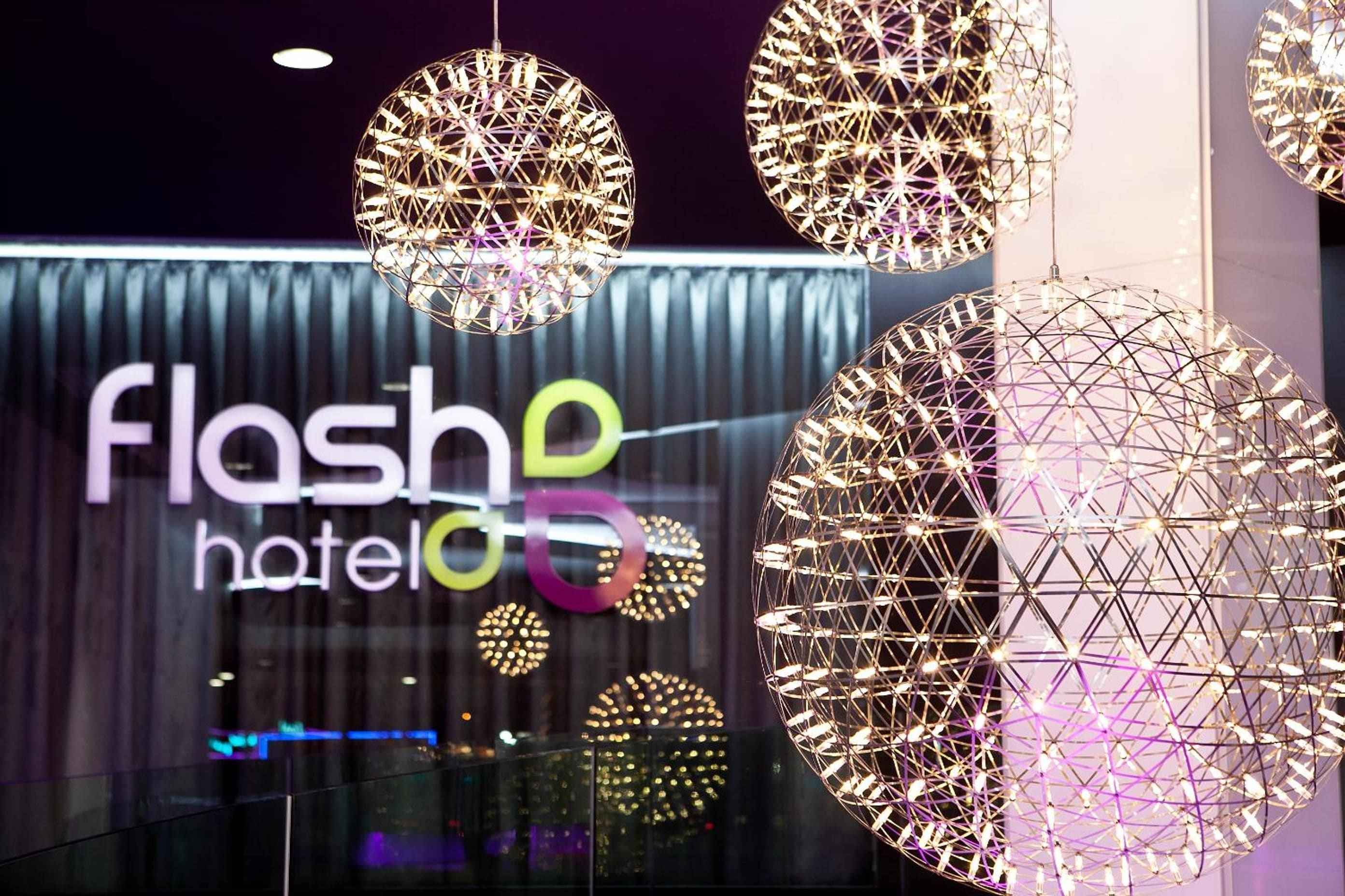 A hotel interior with spherical hanging light fixtures and a modern wall with illuminated letters spelling 'flash hotel'.