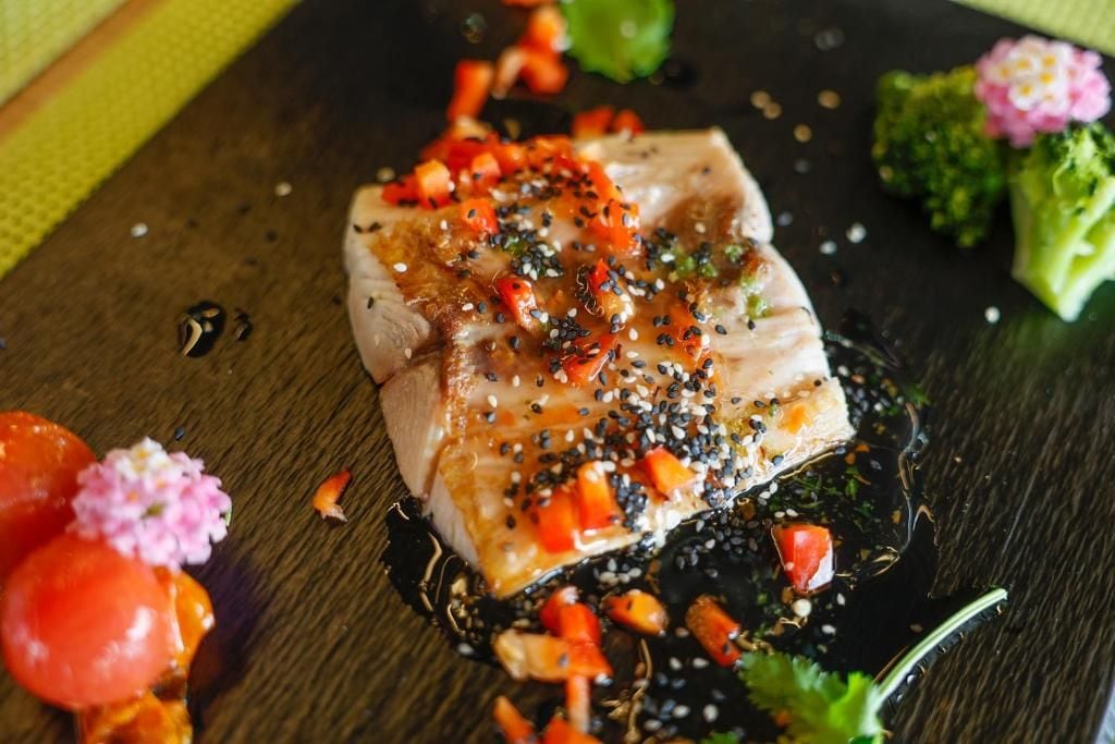 A dish with fish, sesame seeds, and diced vegetables on a dark plate.