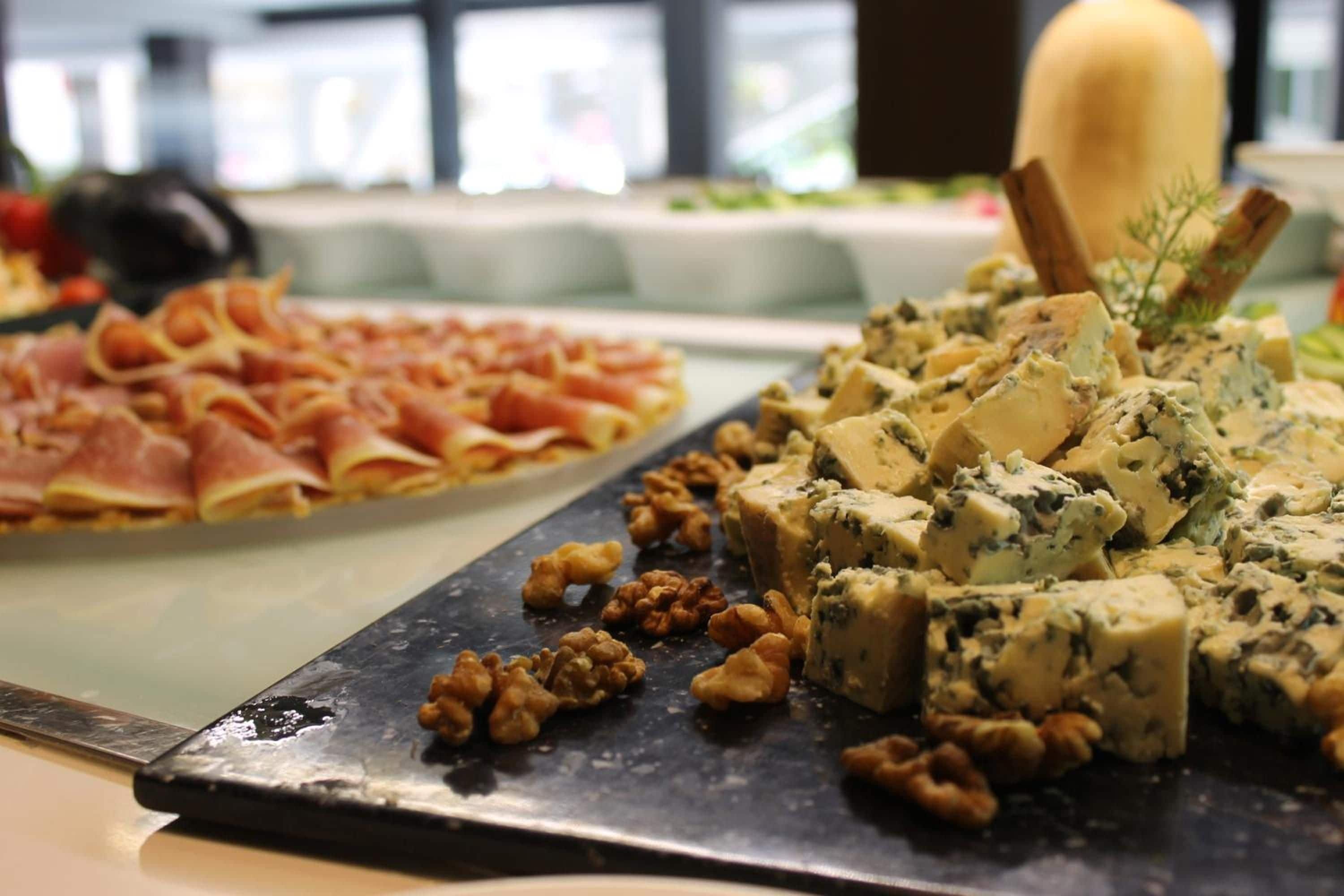 A buffet table with a variety of food items including a platter of sliced meats and a selection of cheeses and nuts.
