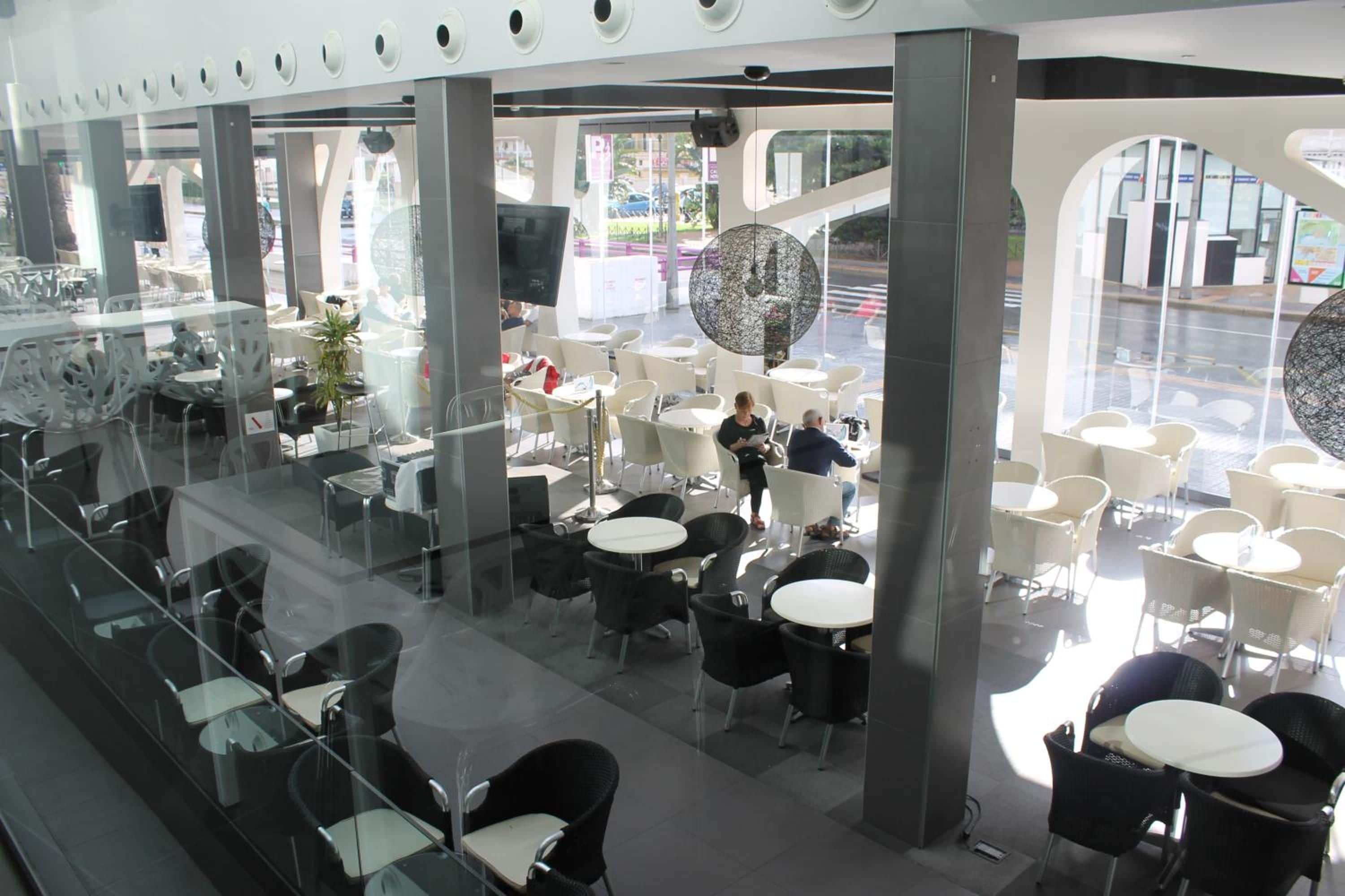 A modern indoor cafe with glass partitions, white tables, and black chairs.