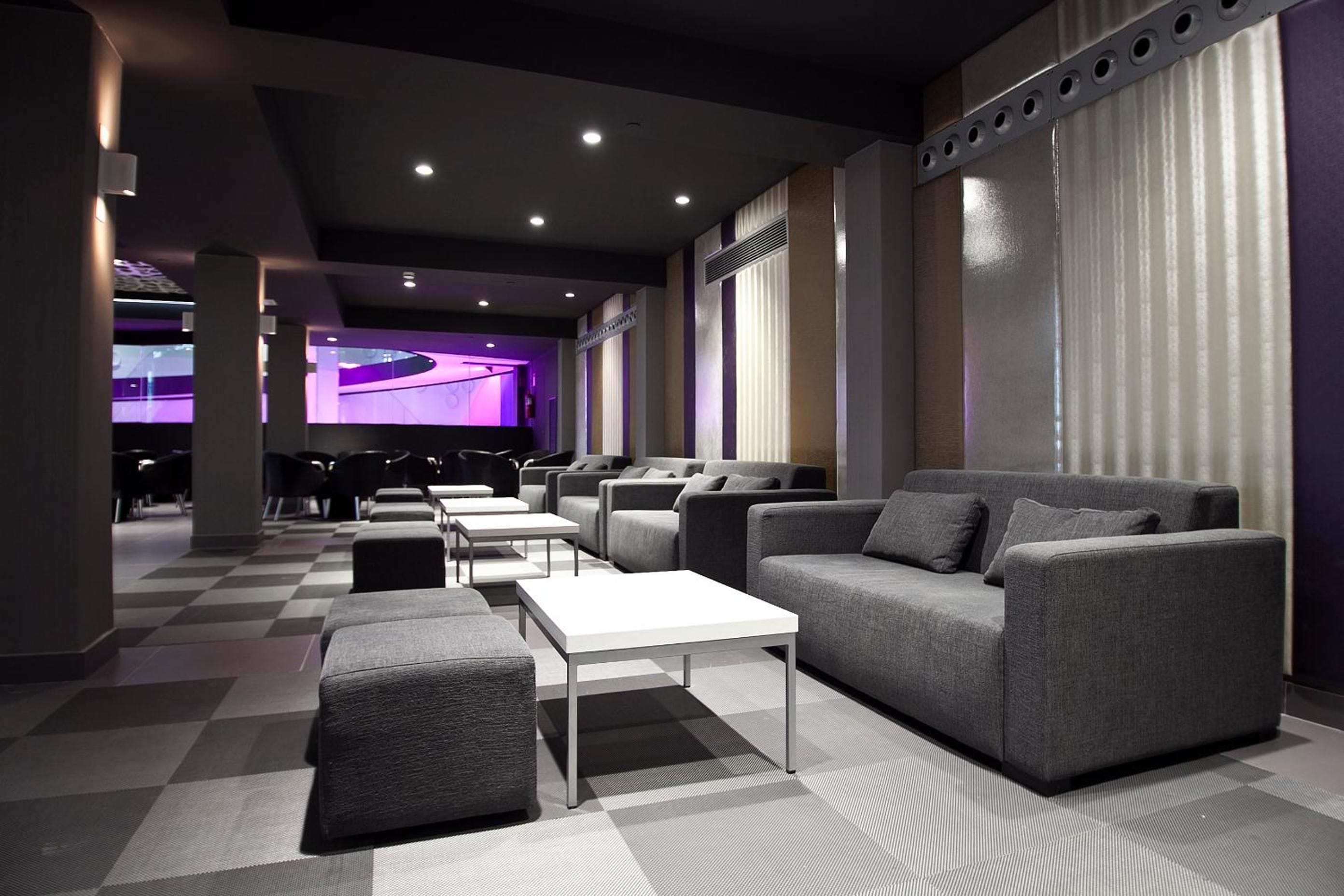 A modern lounge area with seating, tables, and a large screen.