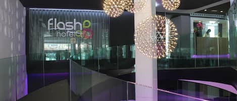 A modern hotel interior with a glass railing, a visible reception desk, and geometric light fixtures.