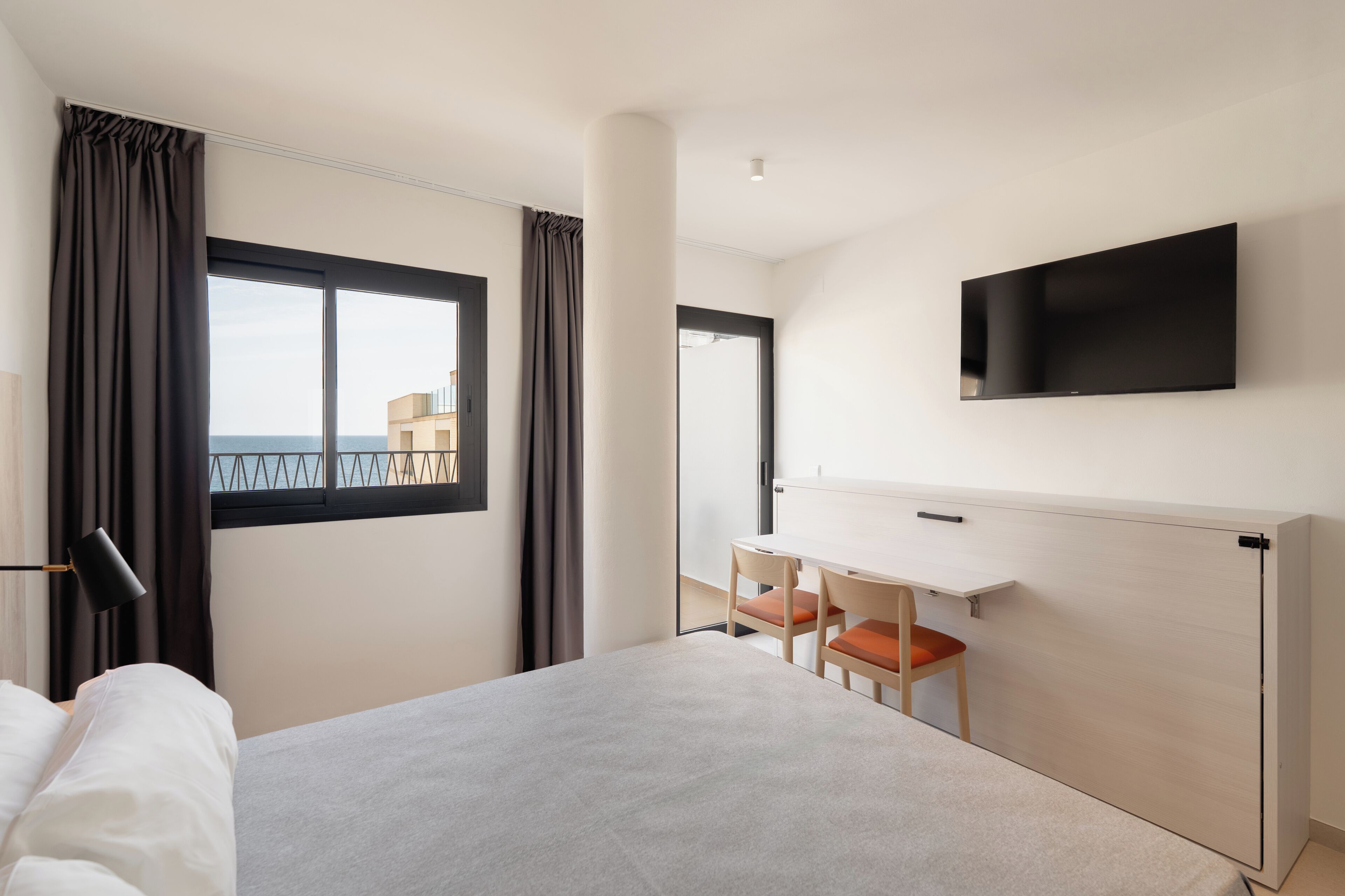 Habitación de hotel con cama, escritorio, silla, televisor montado en la pared y vista al exterior.