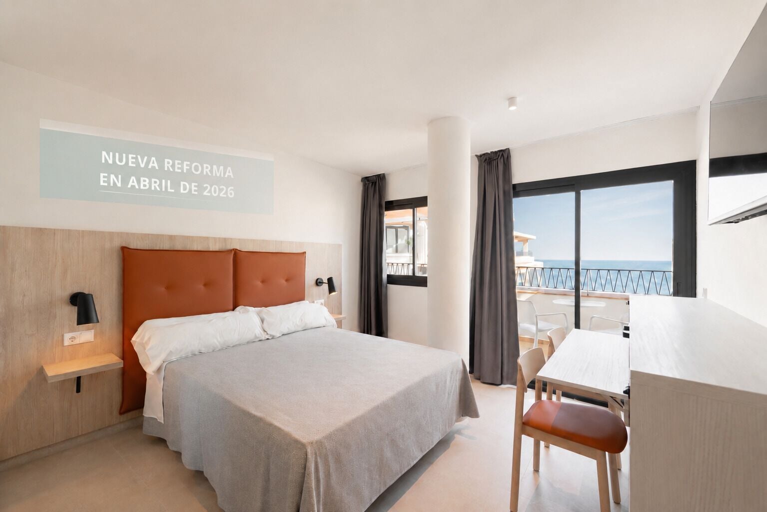 Une chambre d’hôtel comprenant un lit, un bureau, une chaise, un balcon avec vue et un panneau indiquant qu’une nouvelle réforme entrera en vigueur en avril 2026.