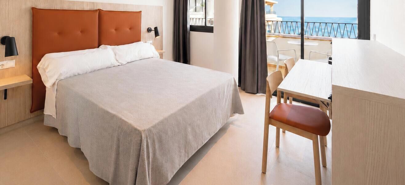 Habitación de hotel con cama, escritorio y vista al mar.