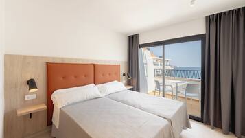 A hotel room with a bed, a nightstand, a desk, and a balcony with a view.