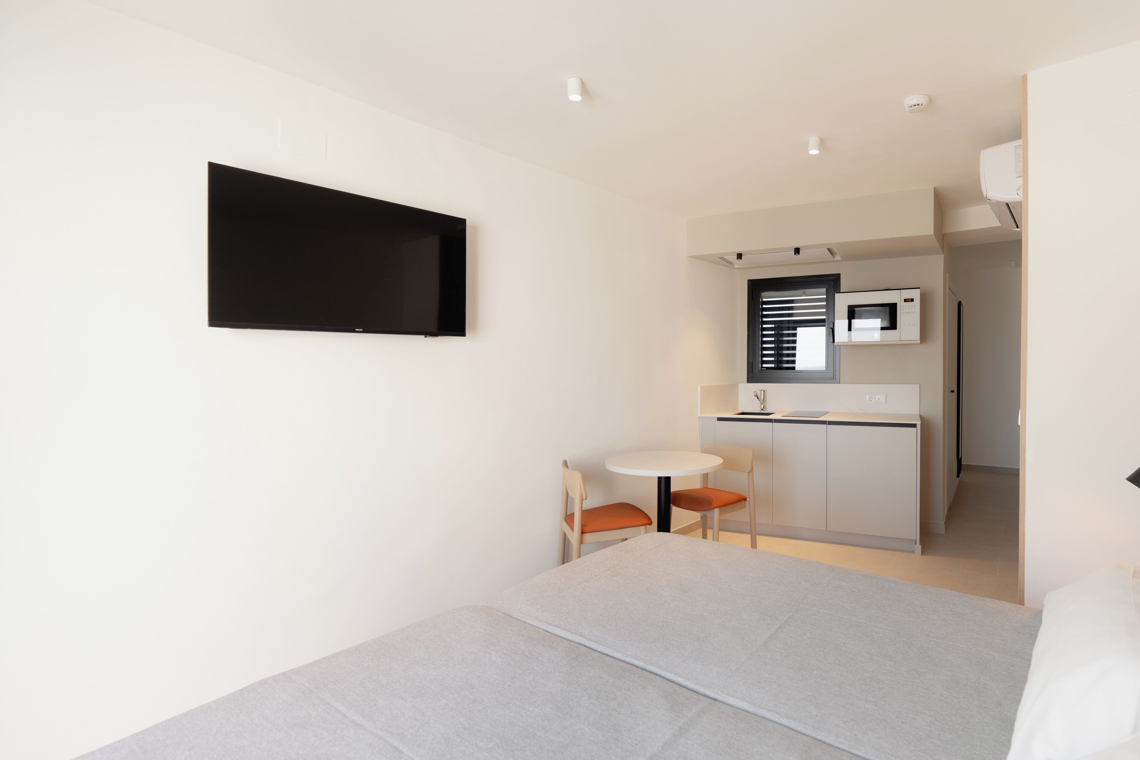 Una habitación de hotel moderna con cama, televisión, una pequeña zona de comedor y kitchenette.