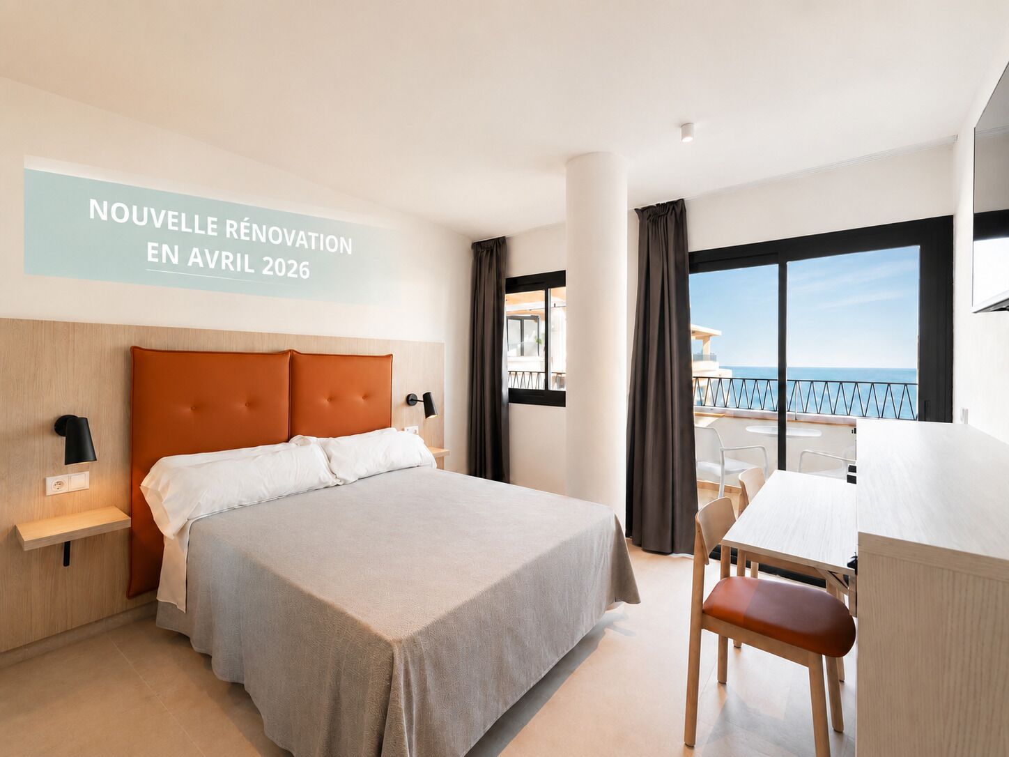 Een hotelkamer met een bed, een bureau en uitzicht op zee.