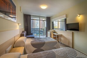 Une chambre d’hôtel avec un lit, un bureau, une chaise, une télévision et une vue sur la ville par la fenêtre.