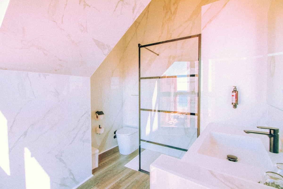 A modern bathroom with a glass shower enclosure, a white sink, and a marble floor.