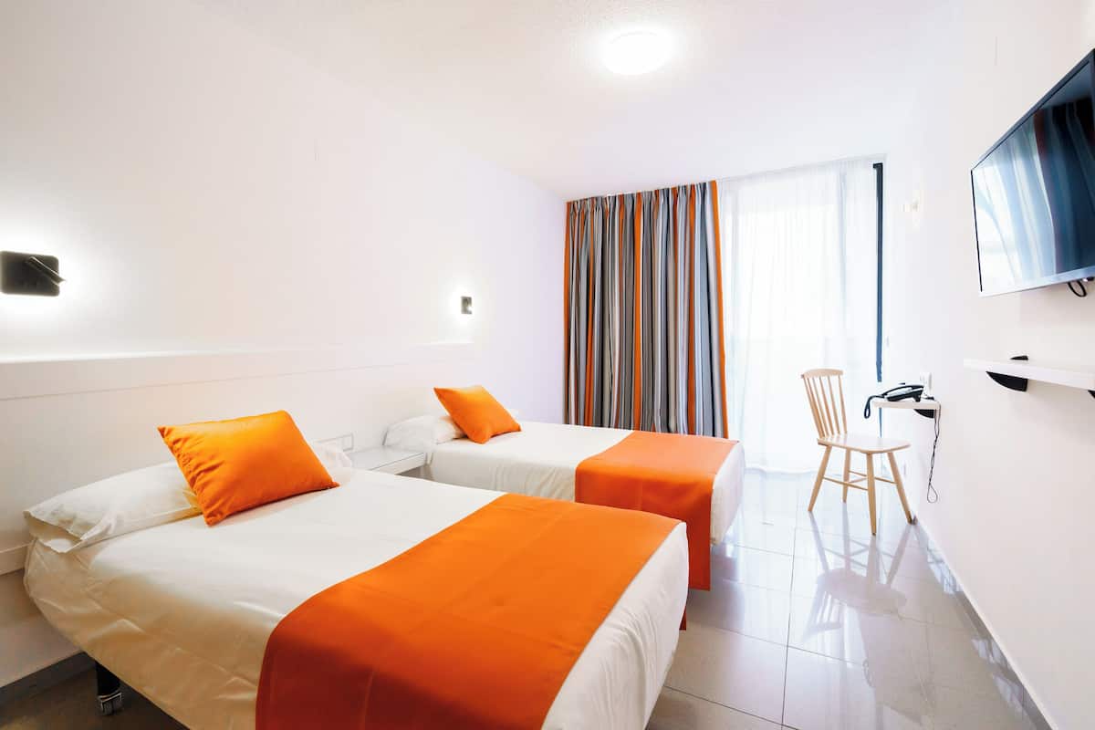 A hotel room with two beds, a desk, a chair, a TV, and a window with curtains.