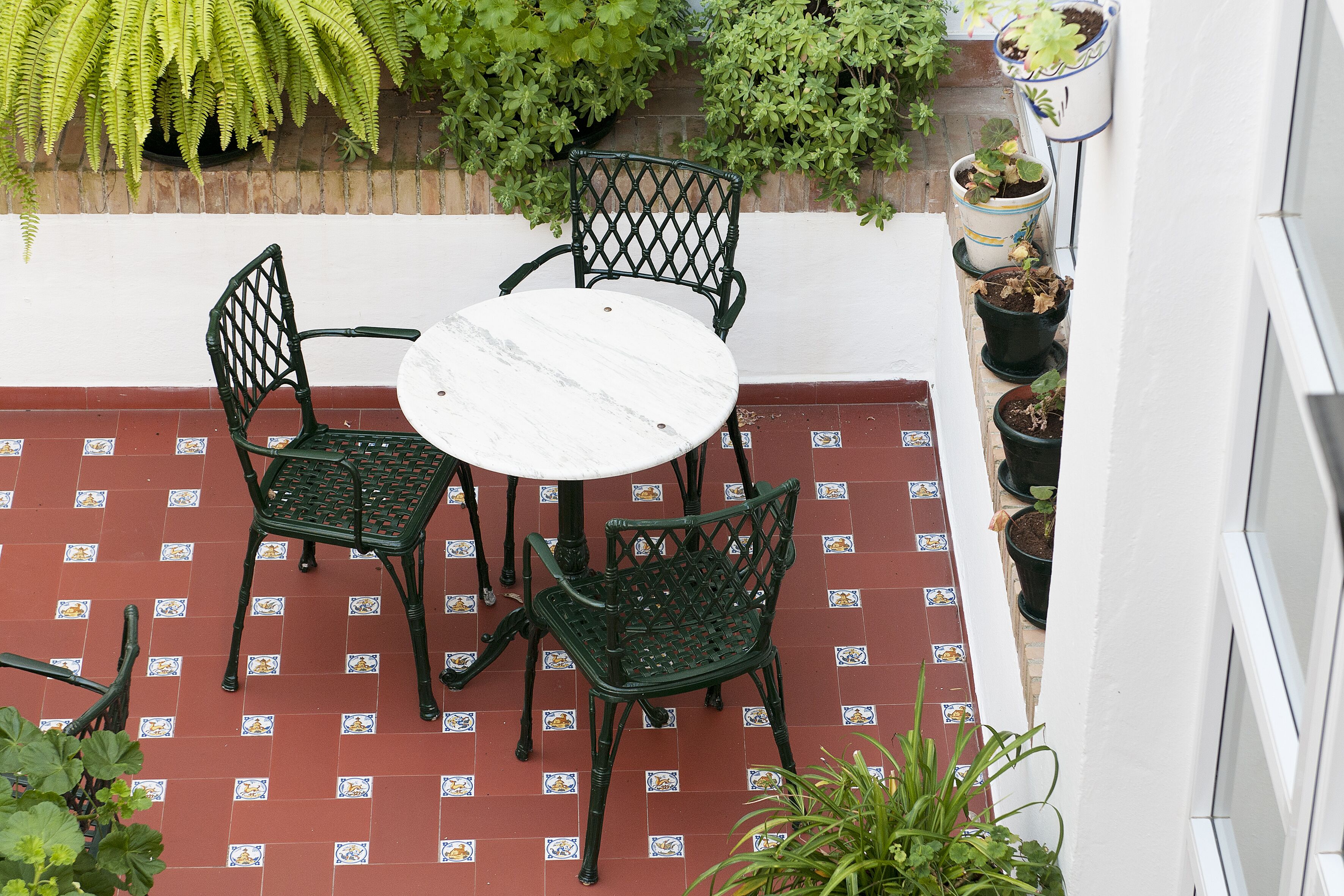Een terras met een ronde tafel en vier stoelen, omgeven door potplanten en een betegelde vloer.
