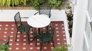 Een terras met een ronde tafel en vier stoelen, omgeven door potplanten en een betegelde vloer.