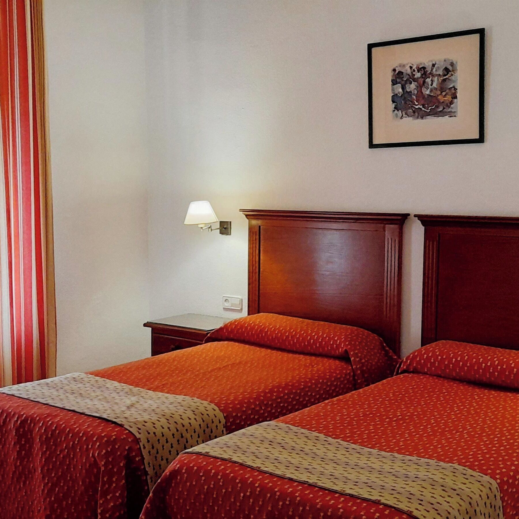 Habitación de hotel con dos camas, una mesita de noche, una lámpara y un cuadro en la pared.