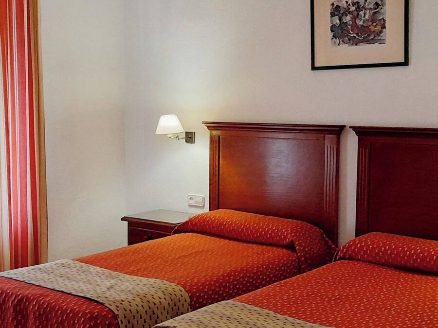 Habitación de hotel con dos camas, una mesita de noche, una lámpara y un cuadro en la pared.