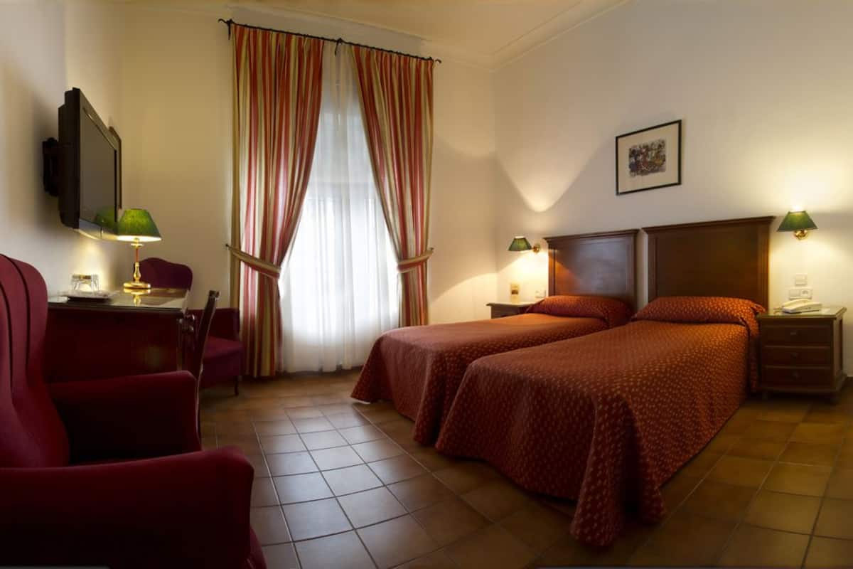 Une chambre d’hôtel avec deux lits, un bureau avec une chaise, une télévision et une fenêtre avec des rideaux.