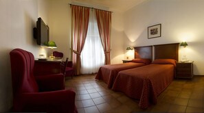 A hotel room with two beds, a desk with a chair, a TV, and a window with curtains.