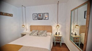 Een slaapkamer met een groot bed, twee nachtkastjes, een spiegel en drie kunstwerken in lijsten aan de muur.
