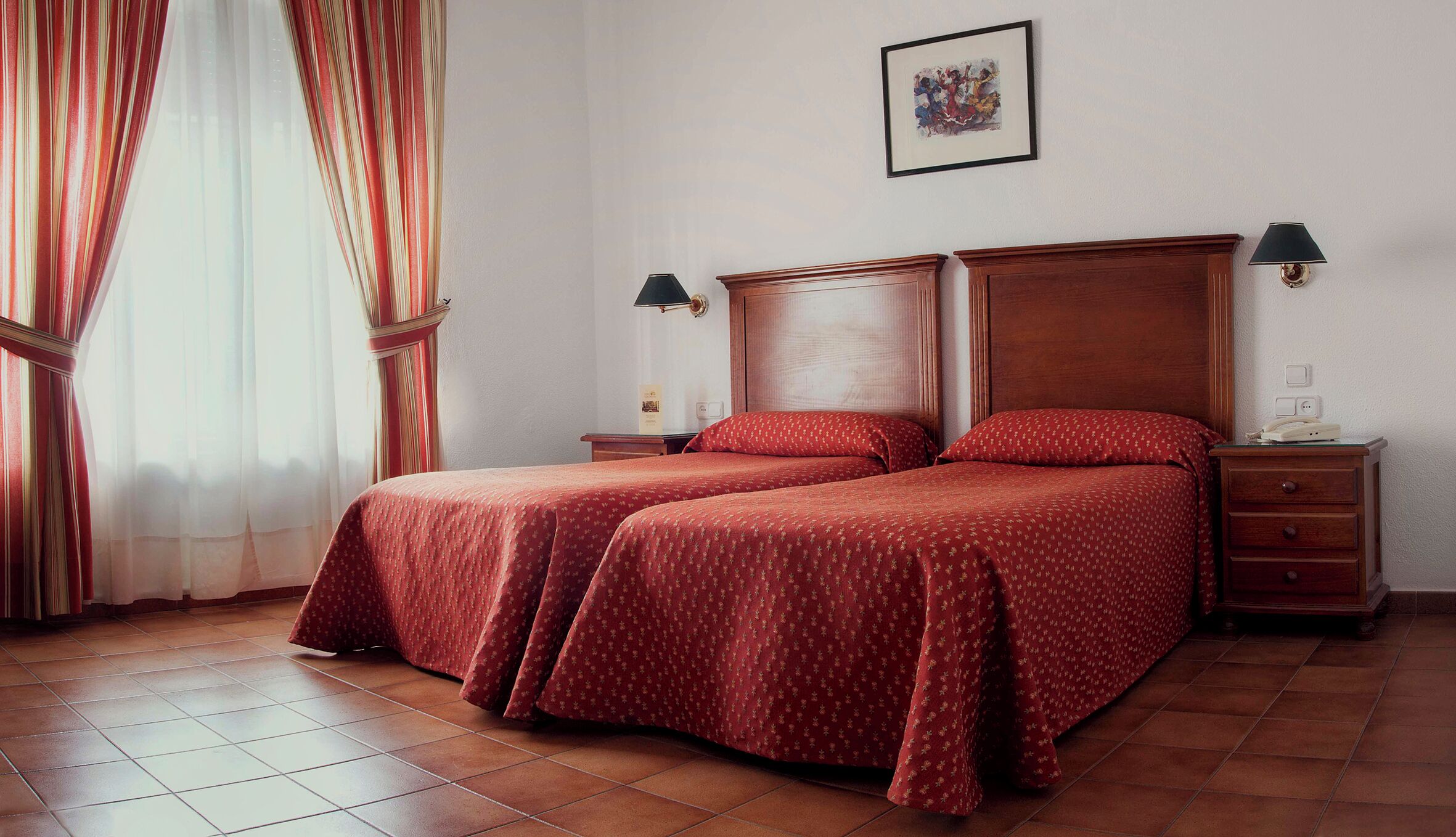 A hotel room with two beds, a wooden headboard, a nightstand with a lamp, and a framed picture on the wall.