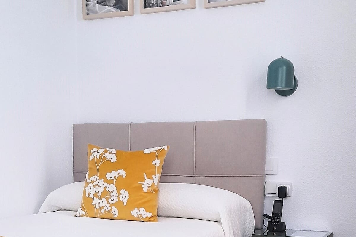 Une chambre d’hôtel bien rangée, avec un lit, une table de chevet dotée d’une lampe et trois tableaux encadrés accrochés au mur.