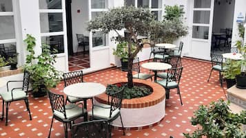 Een binnentuin met buitenmeubilair, plantenpotten en een centrale boom.