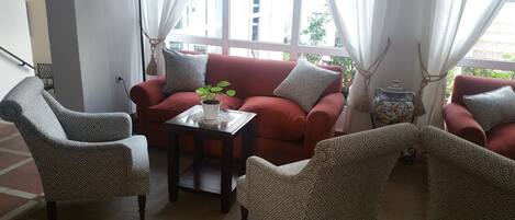 A cozy living room with a red sofa, patterned armchairs, and a small table with a plant.