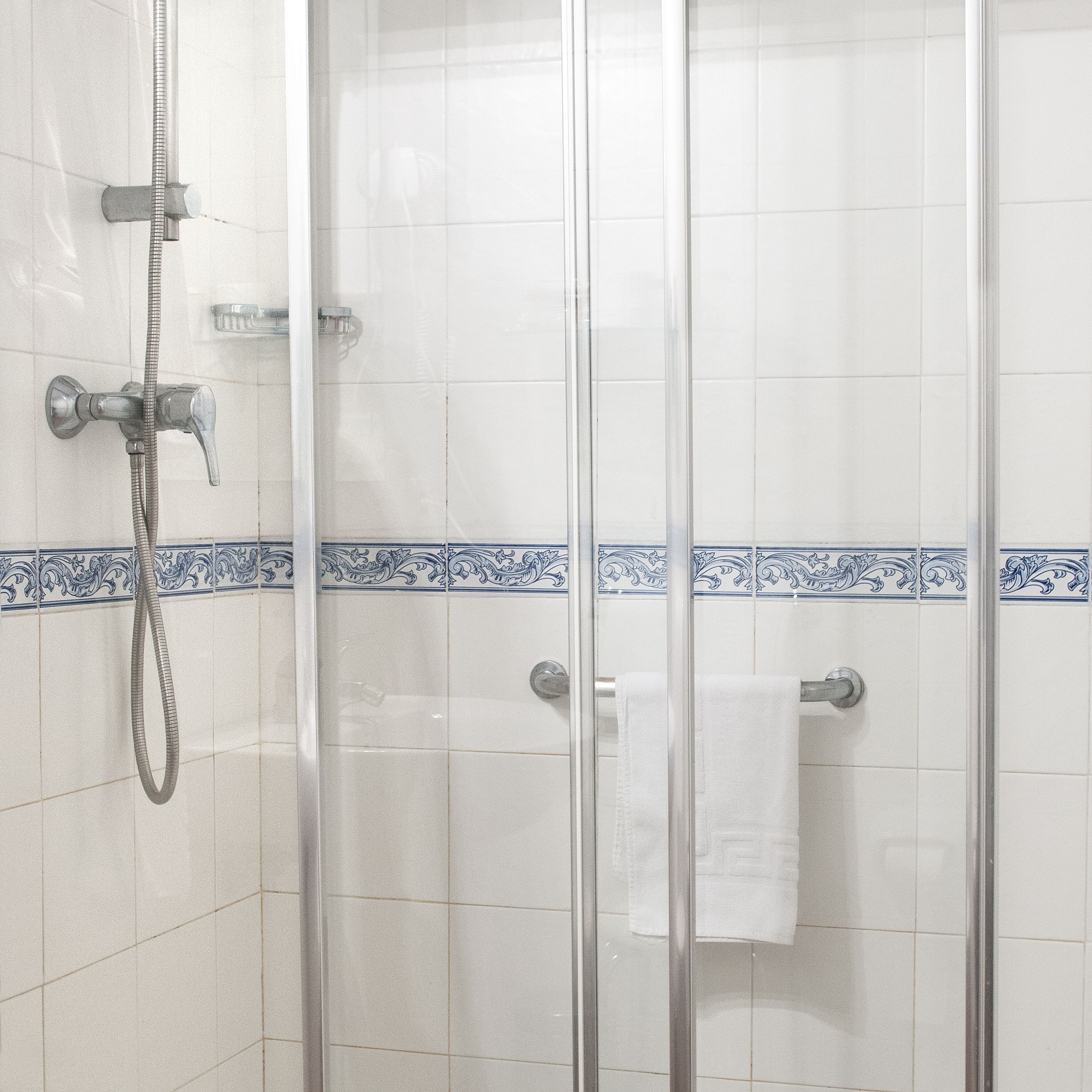 A shower enclosure with a glass door, a handheld showerhead, and a towel rack with a white towel.