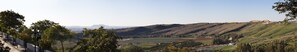 A panoramic view of a hilly landscape with a historic building on a hill, a pathway, and a distant mountain.