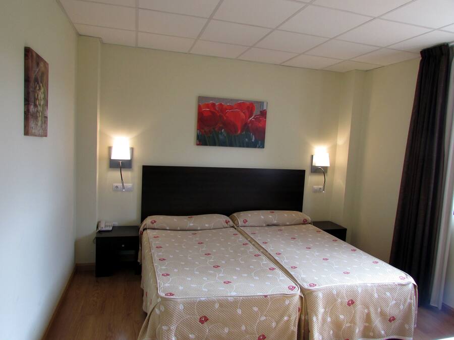 Ein Hotelzimmer mit einem Bett, zwei Nachttischen, einer Wandlampe und einem Gemälde.