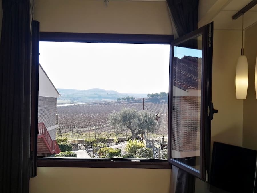 A room with a large window offering a view of a vineyard and distant hills.