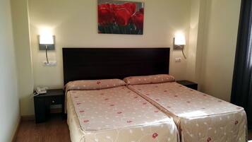 Una cama doble con ropa de cama floral, lámparas de noche y un teléfono instalado en la pared.