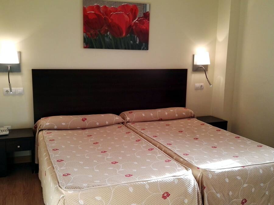 Una cama doble con ropa de cama floral, lámparas de noche y un teléfono instalado en la pared.