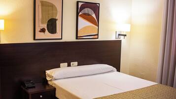A hotel room with a bed, a nightstand, a telephone, and two framed artworks on the wall.