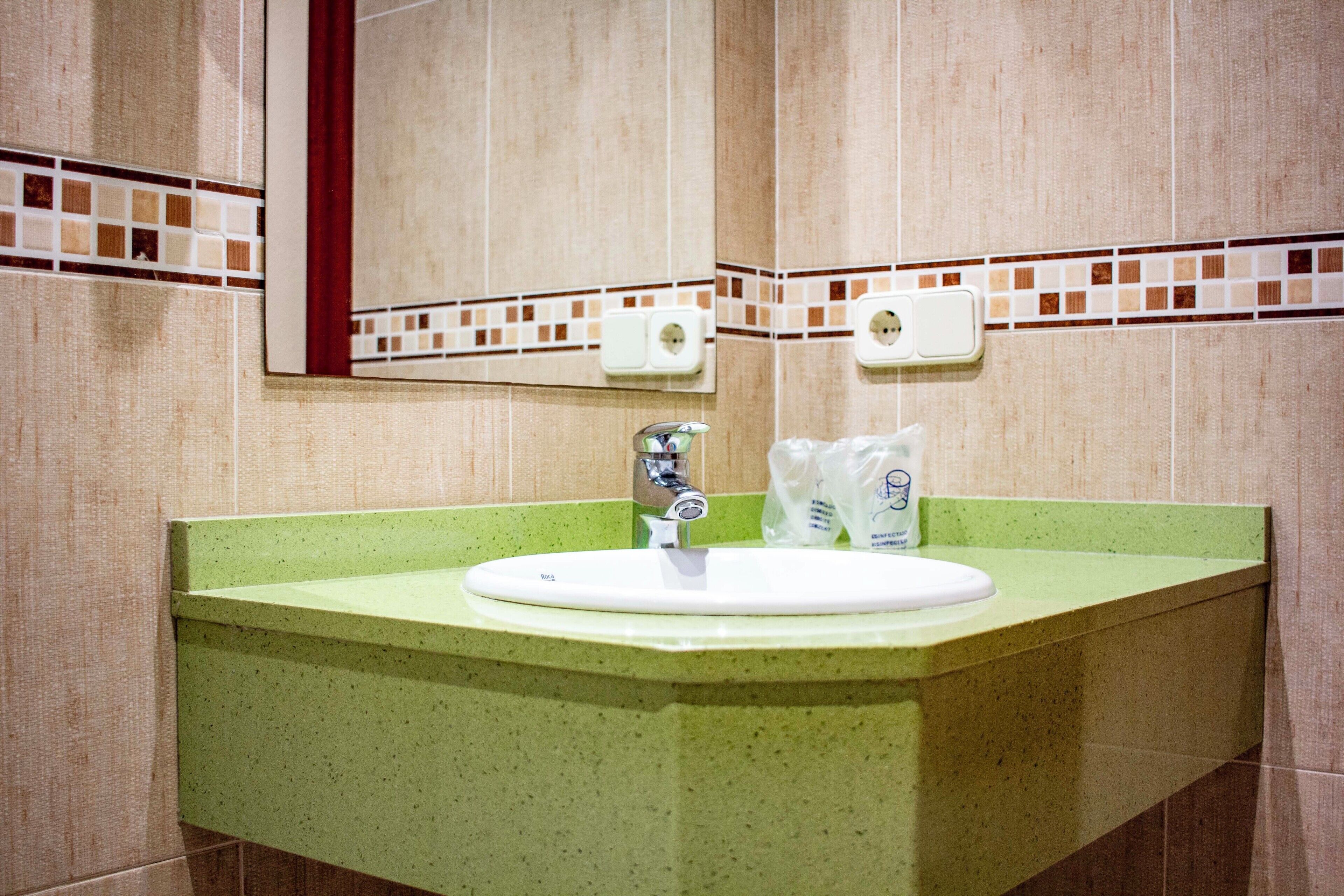 Een badkamer met een groene wastafel, een spiegel en twee zeepdispensers.
