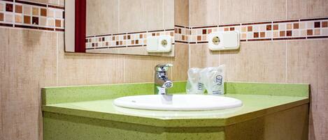 A bathroom with a green sink, a mirror, and two soap dispensers.
