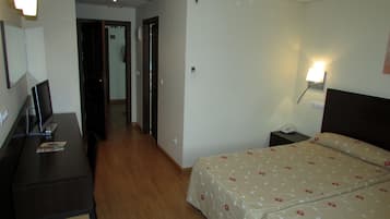 Una habitación de hotel con cama, mesita de noche, lámpara y escritorio con monitor de computadora.
