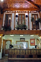 Un vestíbulo de hotel con techo de madera, un mostrador de recepción y un balcón con plantas en macetas.