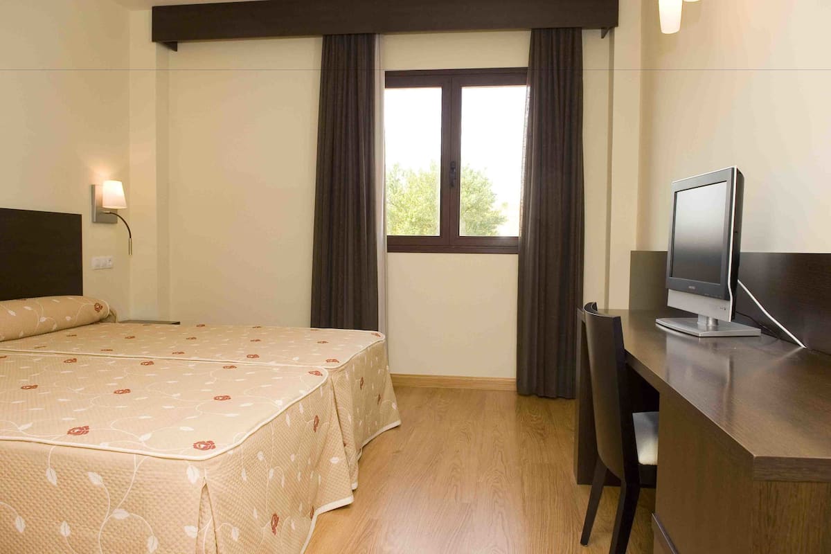 A hotel room with a bed, a desk with a computer, and a window with curtains.