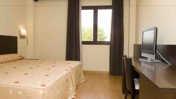 Una habitación de hotel con una cama, un escritorio con computadora y una ventana con cortinas.